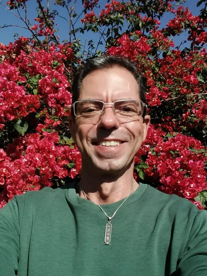 Caio Gracco, terapeuta integrativo, sorrindo ao ar livre diante de uma buganvília florida